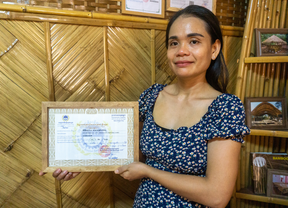 The photo of woman holding framed certificate in front of bamboo interior backround